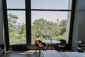 A room with a large window, two chairs, a small table, and a bed. - Hotel Alexander (Mexico City)