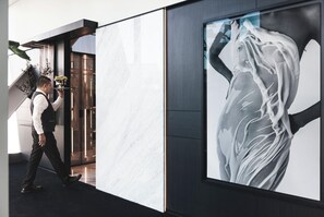 Un moderno vestíbulo de hotel con un mostrador de recepción de mármol, una gran obra de arte abstracta y una escalera.