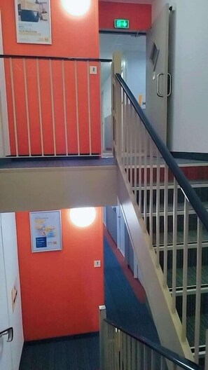 Interior com vários níveis, parede vermelha, escada e tapete azul.