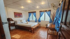 Un dormitorio con cama, mesita de noche, una silla, ventana con cortinas, ventilador de pared y ventilador de techo.