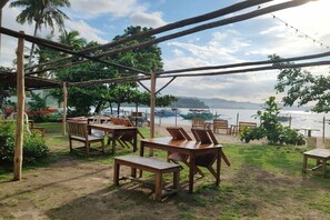 Een terras met houten tafels en stoelen, een pergola en uitzicht op het water en boten.