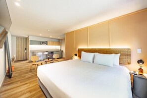 A hotel room with a large bed, a desk, a chair, and a kitchenette. - The Somos Flats Central Poblado (Medellín)