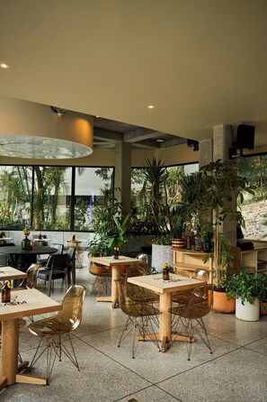 A modern restaurant interior with tables, chairs, and potted plants. - The Somos Flats Central Poblado (Medellín)