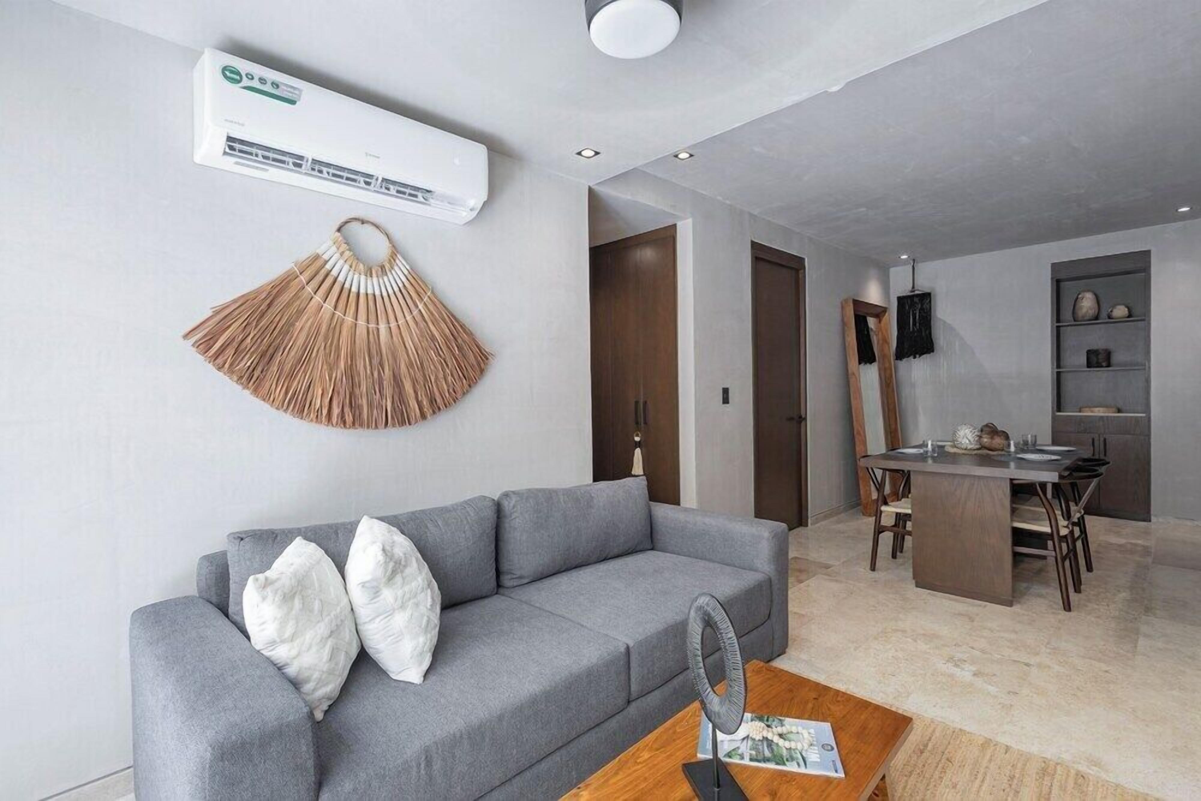 A modern living room with a grey sofa, a fan, and a dining area with a wooden table and chairs.