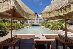 Un espace piscine agrémenté de chaises longues en bois et de parasols en chaume, le tout entouré d’une végétation luxuriante.