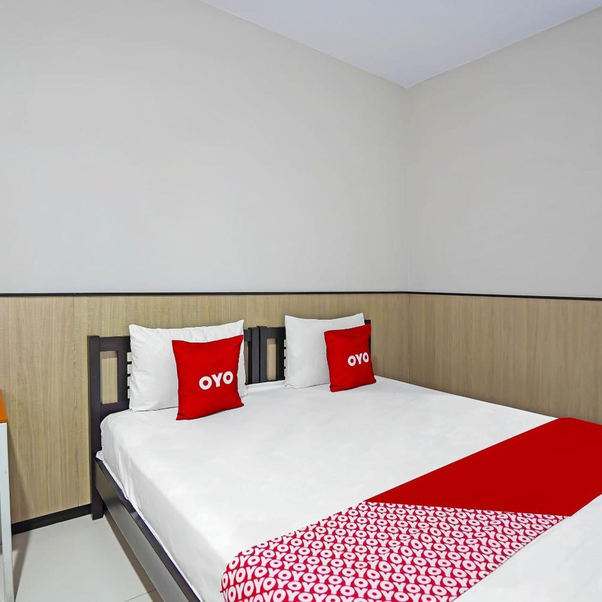 A hotel room with a bed, two pillows with the logo 'OYO', and a red blanket.
