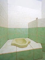 Un baño pequeño con azulejos, que presenta un inodoro pedestal en el centro, rodeado de baldosas verdes y blancas.