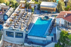 Una piscina sul tetto con lettini e ombrelloni, circondata da edifici e vegetazione.