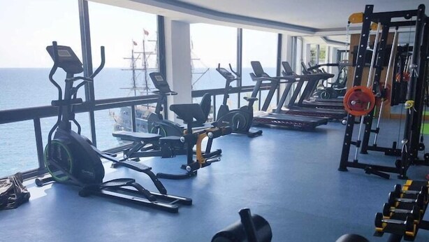 Un gimnasio con diferentes equipos de ejercicio, amplias ventanas y vista al mar.