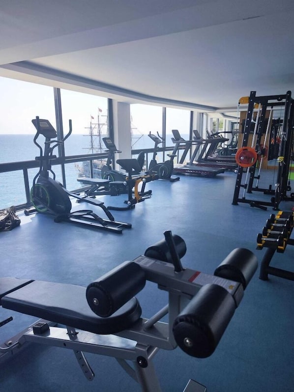 A gym with various exercise equipment, large windows, and a view of the sea.