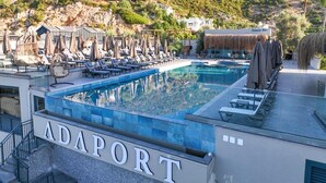 Un área de piscina en la azotea con sillones de descanso y sombrillas, rodeada por un paisaje montañoso.