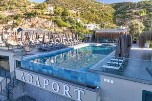 Un área de piscina en la azotea con sillones de descanso y sombrillas, rodeada por un paisaje montañoso.