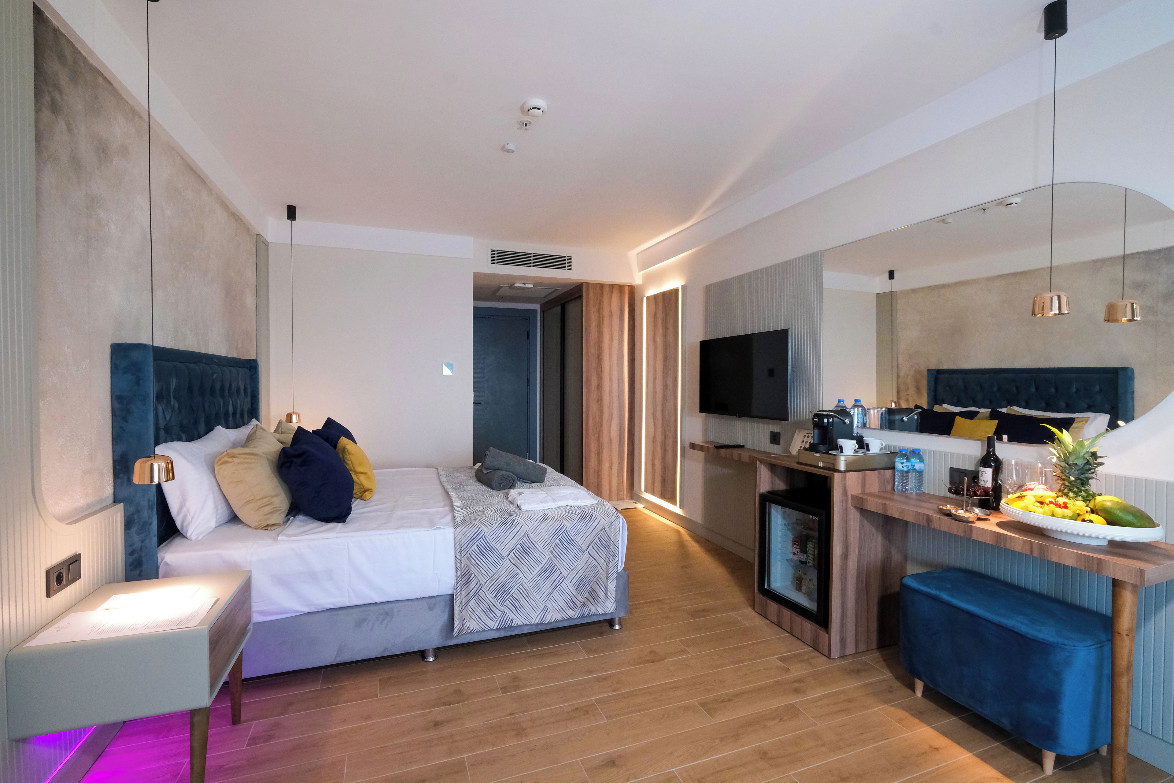 A modern hotel room with a bed, bedside table, and a small kitchenette.