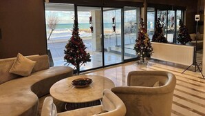Rebedor modern d'hotel amb una finestra gran que ofereix vista a la platja, dos arbres de Nadal i un penjador de cristall.