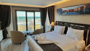 Habitació d'hotel amb un llit gran, vista al mar, un quadre a la paret i una taula petita amb una cadira.