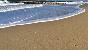 Una platja amb ones que s'estrep a la riba, un cel serè i un moll de pedra a la distància.