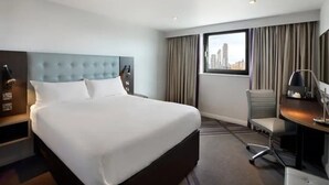 A hotel room with a large bed, a desk, a chair, and a view of the city through the window. - Premier Inn Cambridge City Centre (Cambridge)