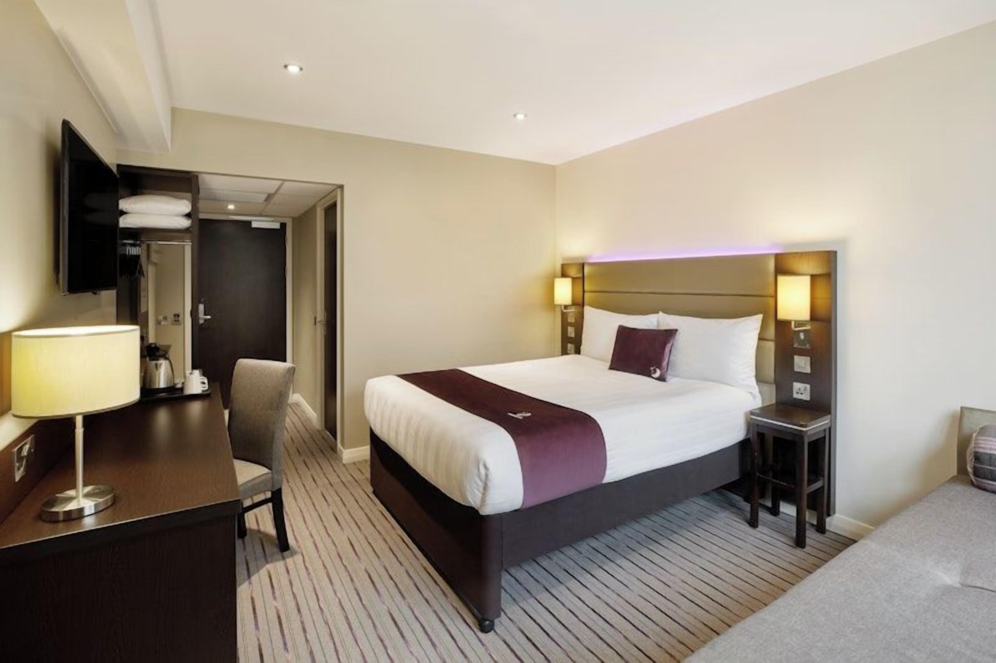 A hotel room with a bed, bedside tables, a desk with a lamp, a chair, and a wardrobe.