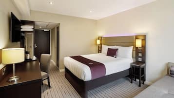 A hotel room with a bed, bedside tables, a desk with a lamp, a chair, and a wardrobe.