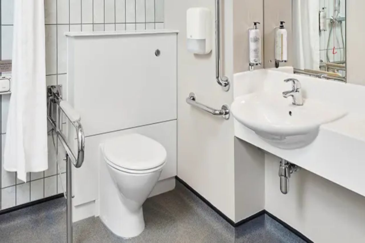 A modern bathroom with a white toilet, a sink with a mirror, and a hand sanitizer dispenser.