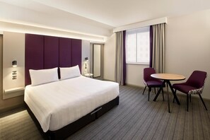 A hotel room with a large bed, a round table, two chairs, a mirror, and a window with curtains. - Premier Inn Cambridge City Centre (Cambridge)