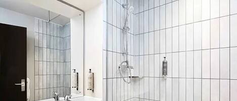 A modern bathroom with white tiled walls, a large mirror, two sinks, and a shower.