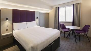 A hotel room with a large bed, a desk, two chairs, and a window with curtains.