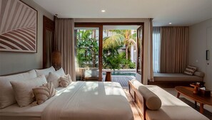 A modern bedroom with a large bed, a seating area, and a view of a tropical garden. - Cocana Resort (Gili Trawangan)