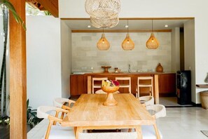 Un coin repas avec une table en bois, des chaises en osier et un grand saladier de fruits placé au centre.