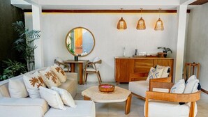 A modern living room with a sofa, armchairs, a coffee table, and a wooden cabinet. There are three wicker pendant lights hanging above the cabinet. - Cocana Resort (Gili Trawangan)