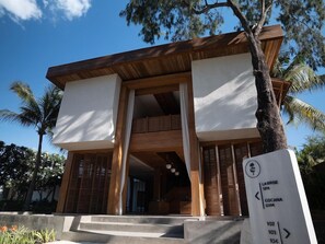 Un bâtiment moderne doté d’une façade en bois et de grandes fenêtres. Une enseigne indique les directions pour se rendre au spa « La Brise » et à la salle de sport « Cocana ».