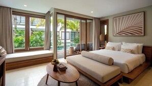 A modern hotel room with a large bed, a sofa, a small table with fruit, and a view of a pool and greenery. - Cocana Resort (Gili Trawangan)