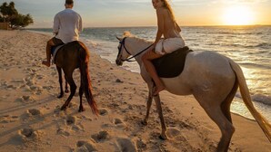 Two people riding horses on a beach with the ocean in the background. - Cocana Resort (Gili Trawangan)