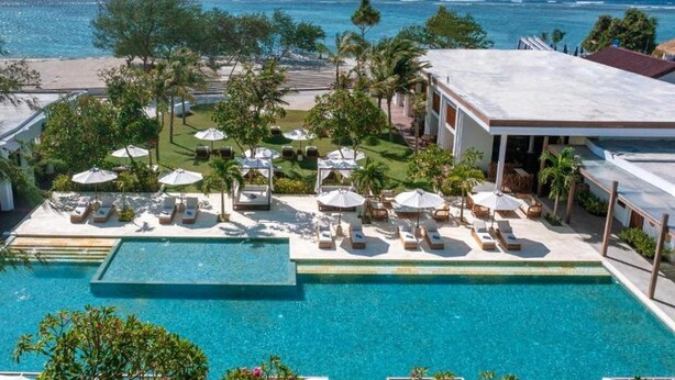 A pool area with lounge chairs and umbrellas, a view of the ocean, and a building with a flat roof. - Cocana Resort (Gili Trawangan)