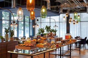 A breakfast buffet with various food items and beverages, modern lighting fixtures, and large windows allowing natural light. - Hotel Indigo Coventry (Coventry)