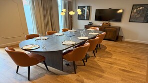 A dining area with a long table set for six, surrounded by six chairs, a television on the wall, and a wooden cabinet. - Hotel Indigo Coventry (Coventry)