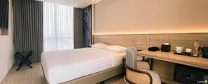 Una habitación de hotel con cama, escritorio, silla, cafetera y minibar.