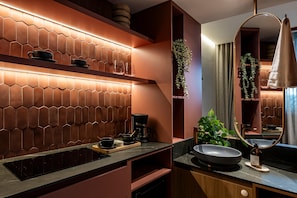 A modern bathroom with a hexagonal tile backsplash, a coffee machine, a sink with a round basin, and a large mirror. - Heiss Hotel (Medellín)