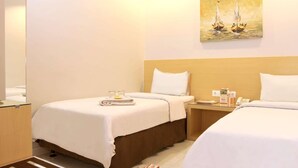 A hotel room with two beds, a painting of sailboats on the wall, a bedside table with a lamp, and a small table with toiletries. - Hotel Grande Lampung Powered by Archipelago (Bandar Lampung)