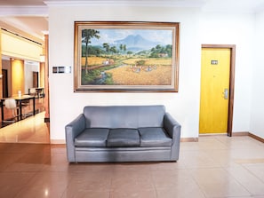 Un hall d’entrée avec un canapé gris, un tableau de paysage encadré, un panneau « interdiction de fumer » et une porte portant le numéro 101.