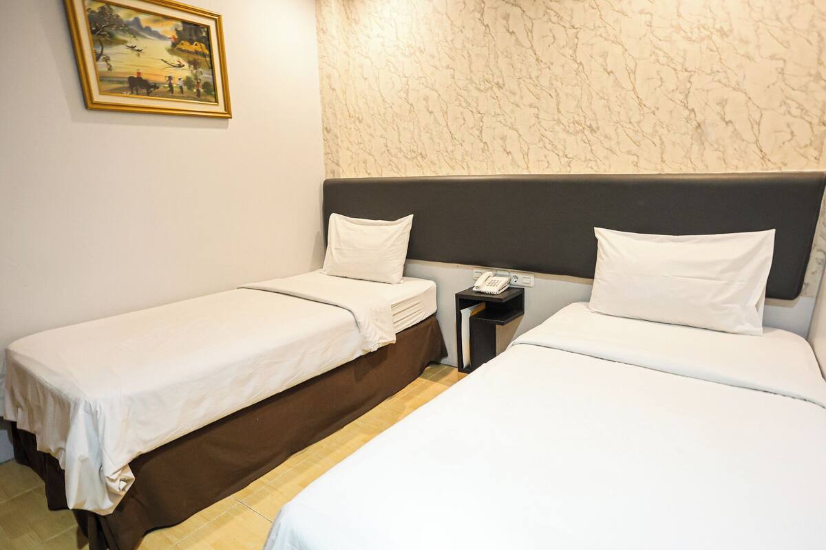 Een hotelkamer met twee enkele bedden, een nachtkastje met een telefoon, en een schilderij aan de muur.