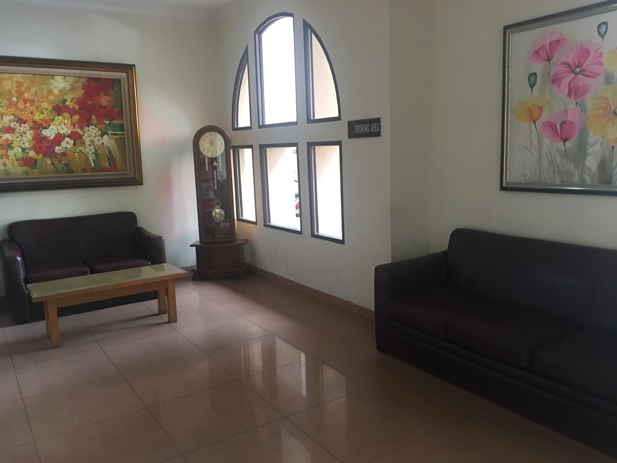 A room with a sofa, a bench, a clock, a painting, and a sign indicating a smoking area.