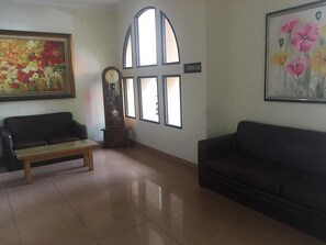 A room with a sofa, a bench, a clock, a painting, and a sign indicating a smoking area. - Hotel Grande Lampung Powered by Archipelago (Bandar Lampung)