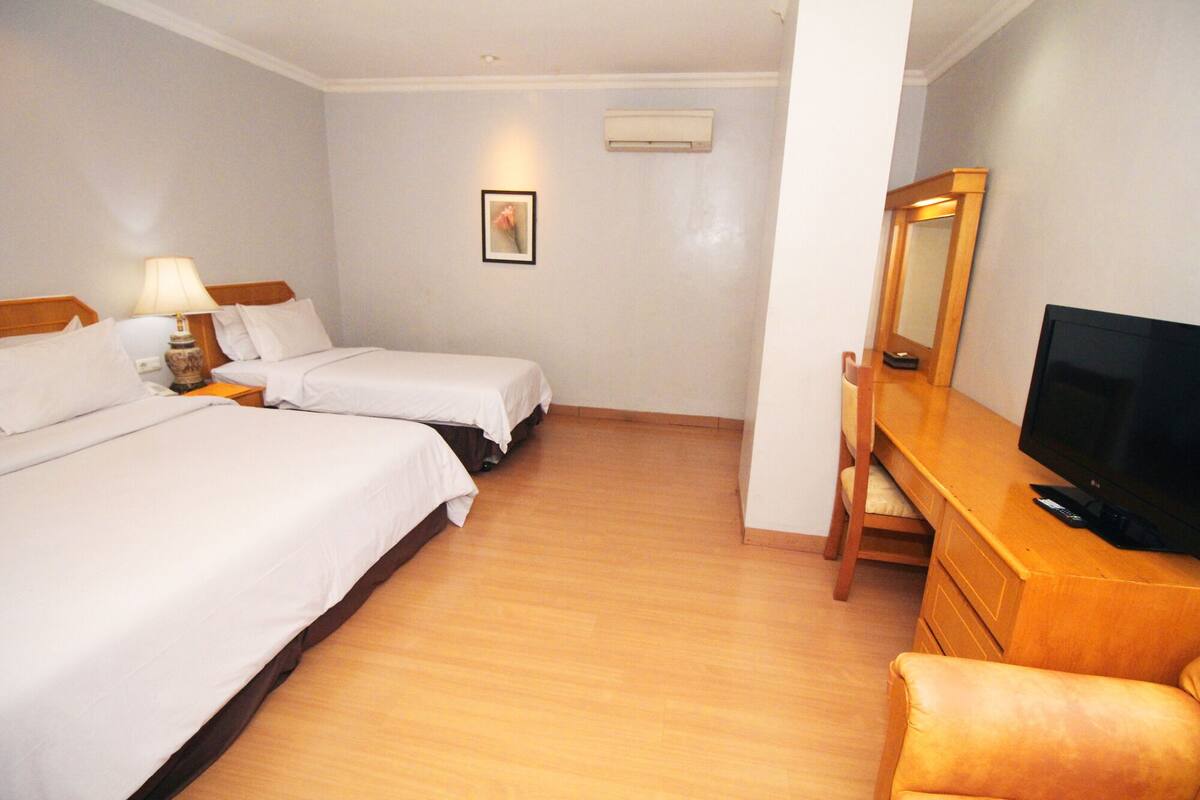 Een hotelkamer met twee bedden, een bureau met een televisie, een stoel, een lamp en een schilderij aan de muur.