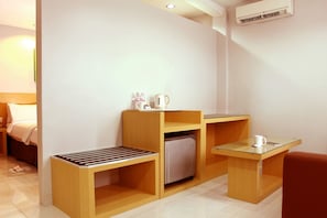 A compact hotel room with a bed, a small kitchenette, a seating area, and a refrigerator. - Hotel Grande Lampung Powered by Archipelago (Bandar Lampung)