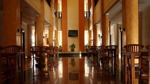 A spacious lobby with a polished floor, wooden chairs, and a television mounted on the wall. - Hotel Grande Lampung Powered by Archipelago (Bandar Lampung)