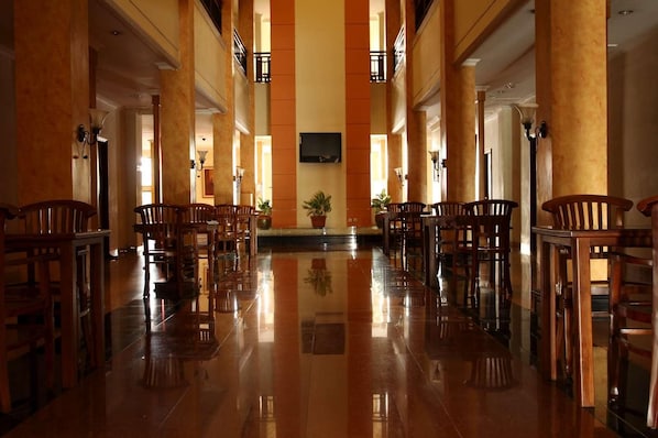 A spacious lobby with a polished floor, wooden chairs, and a television mounted on the wall. - Hotel Grande Lampung Powered by Archipelago (Bandar Lampung)