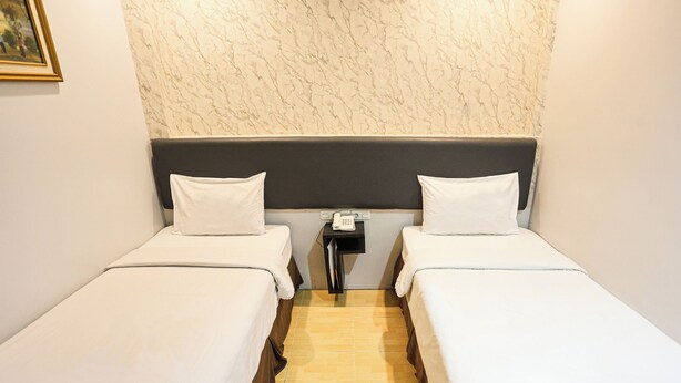 A hotel room with two single beds, a nightstand with a phone, and a marble-patterned wall. - Hotel Grande Lampung Powered by Archipelago (Bandar Lampung)