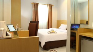 A hotel room with a bed, a desk with a laptop, a chair, a small table with a tray, and a mirror. - Hotel Grande Lampung Powered by Archipelago (Bandar Lampung)