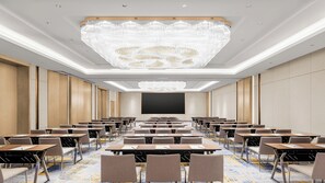 Een congrescentrum met een grote kroonluchter, rijen tafels en stoelen, en een groot scherm aan de voorkant.